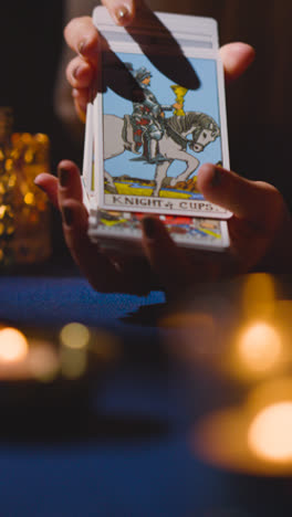 Vertical-Video-Close-Up-Of-Woman-Shuffling-Or-Cutting-Cards-For-Tarot-Reading-On-Candlelit-Table